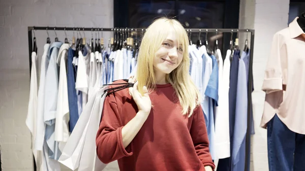 Une jeune femme blonde souriante et heureuse vient d'acheter des vêtements dans un magasin — Photo