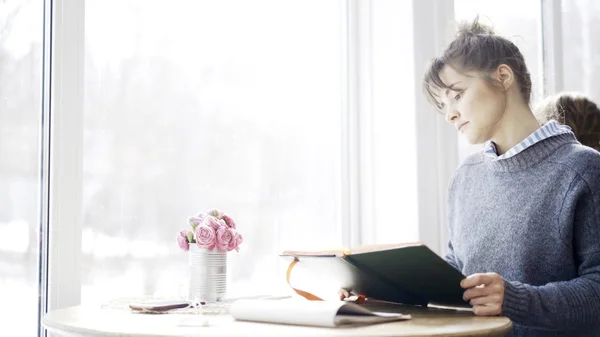 Una giovane ragazza bruna sta tenendo e guardando in un notebook nel caffè — Foto Stock