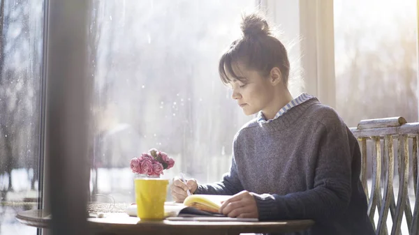 Uma jovem morena está escrevendo notas para um caderno no café — Fotografia de Stock