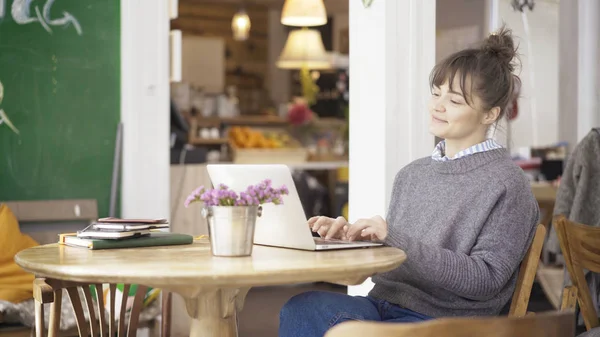 Una joven morena linda sonriente está trabajando con un ordenador portátil en un café — Foto de Stock