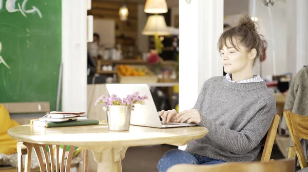 Een lachende schattige brunette meisje is werken met een laptop in een café — Stockfoto
