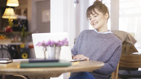 Una joven morena feliz sonriente linda está trabajando con un ordenador portátil en un café — Foto de Stock