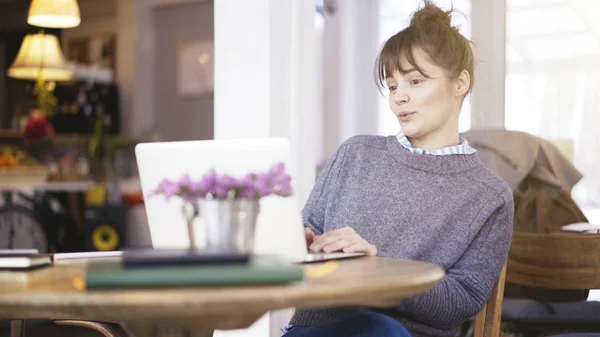 Een jonge verrast schattige brunette meisje is werken met een laptop in een café — Stockfoto