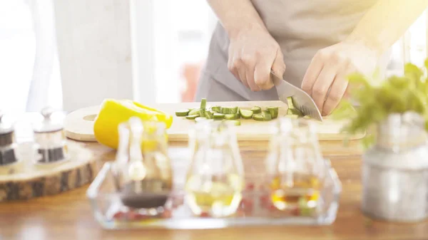 Manliga spisar händer skivning gurkor på en träskiva matlagning — Stockfoto