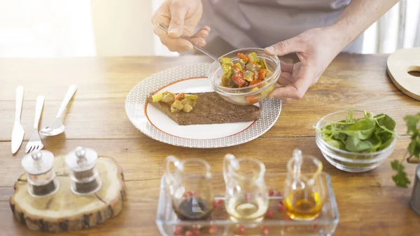 En manlig chef sätter stew sallad på en bit av en svart bröd — Stockfoto