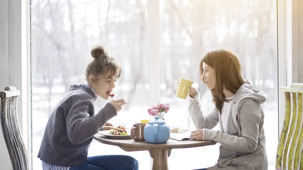 Two adult female friends eating and drinking tea in a cafe