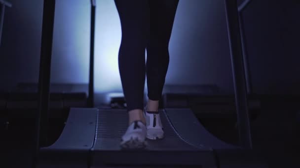 Женские ноги в белых кроссовках и леггинсах бегают на беговой дорожке медленно мо — стоковое видео