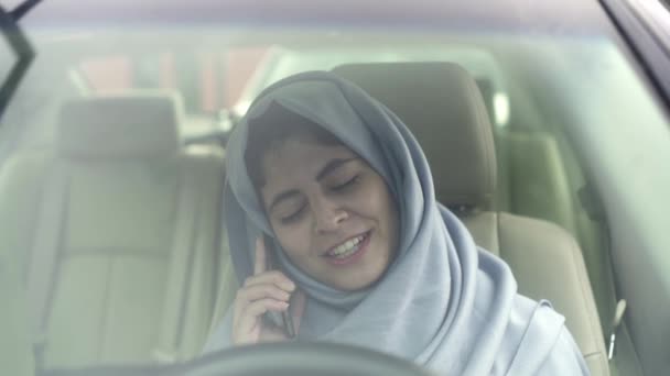 美丽的年轻女子在面纱谈论智能手机在她的车和笑 — 图库视频影像
