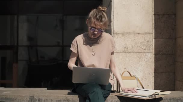 Привлекательная молодая женщина учится с ноутбуком и книгами на улице, летом — стоковое видео