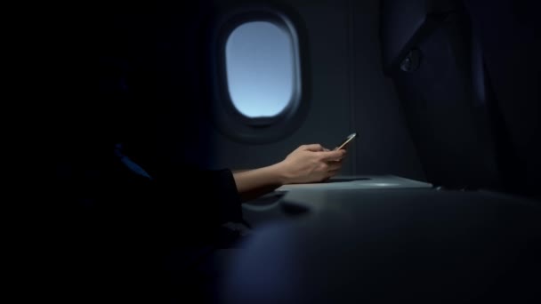 Woman hand typing on her smartphone in a dark plane — Stock Video