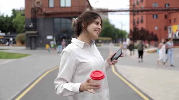 Aantrekkelijke jonge meisje met koffie en smartphone dansen in de straat — Stockvideo