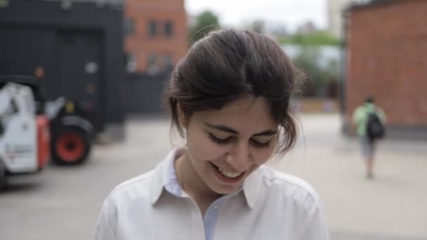 Bescheidenes junges Mädchen mit dunklen Haaren, das auf der Sommerstraße spaziert und lächelt — Stockvideo