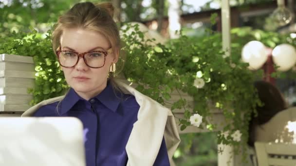 Mujer joven absorbida en gafas de trabajo con ordenador portátil en un café de verano — Vídeo de stock