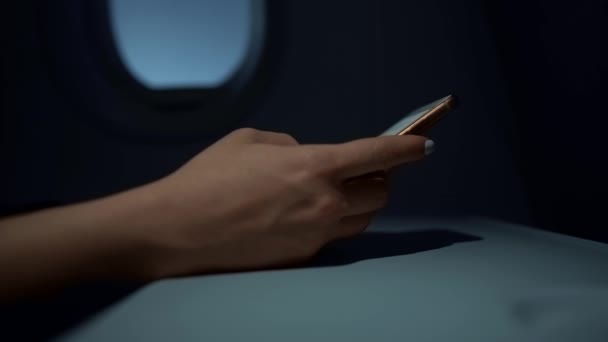 Femme tapant à la main sur son smartphone dans un avion sombre, gros plan — Video