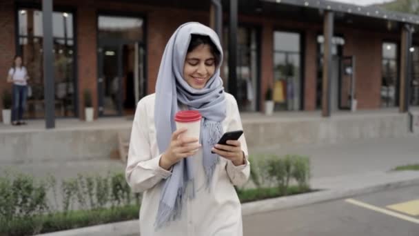 Fiatal nő a kávéfogyasztás és látszó-on smartphone szürke hidzsáb — Stock videók