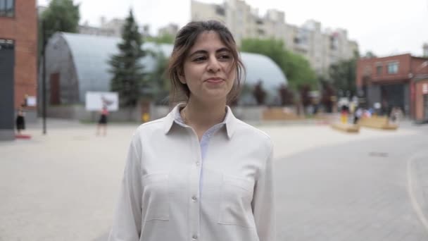 Bescheidene junge Frau mit dunklen Haaren, die auf der Sommerstraße spaziert und lächelt — Stockvideo