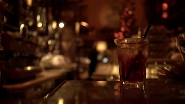 Vaso de bebida alcohólica sobre una mesa de bar, fondo borroso — Vídeo de stock