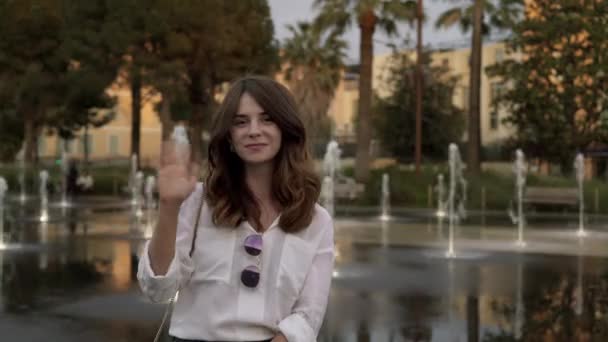 Belle touriste agitant la main debout près d'une fontaine dans la rue française — Video