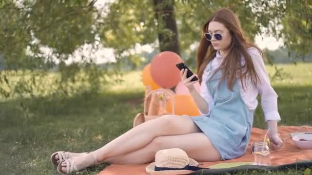 Ginger girl in glasses and jeans skirt making selfie during picnic in park — Stock Video