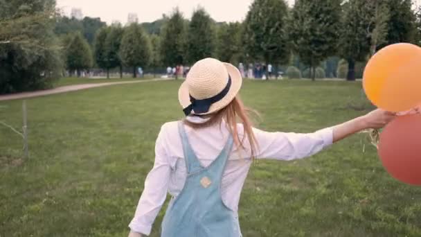 Χαμογελώντας τζίντζερ κορίτσι σε γυαλιά ηλίου τρέξιμο και στροβιλίζονται με μπαλόνια στο πάρκο — Αρχείο Βίντεο
