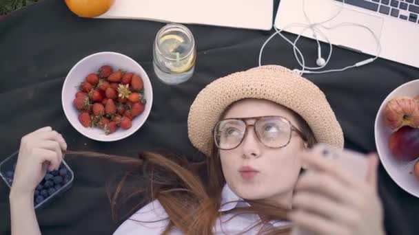 Rood harige jonge vrouw maken van grappige gezichten en selfies in park liggen — Stockvideo