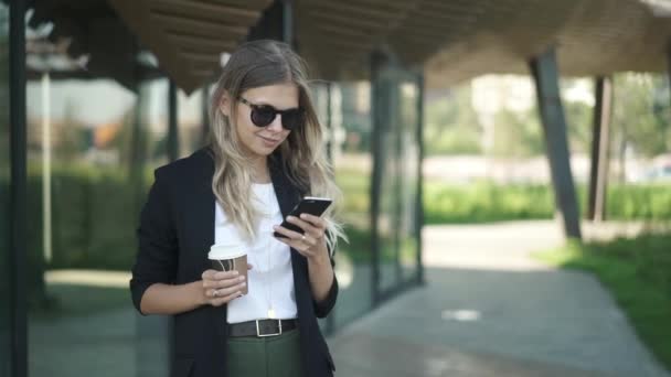 Hermosa mujer rubia con café mirando el teléfono inteligente en verano y sonriendo — Vídeo de stock