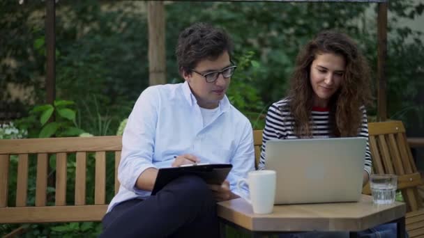 Junge Geschäftspartner diskutieren im Sommer auf Parkbank über ihr Projekt — Stockvideo