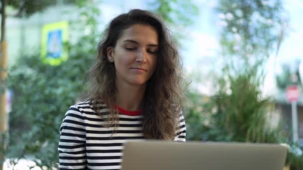Atractivo joven pelo rizado morena trabajando con el ordenador portátil fuera — Vídeo de stock