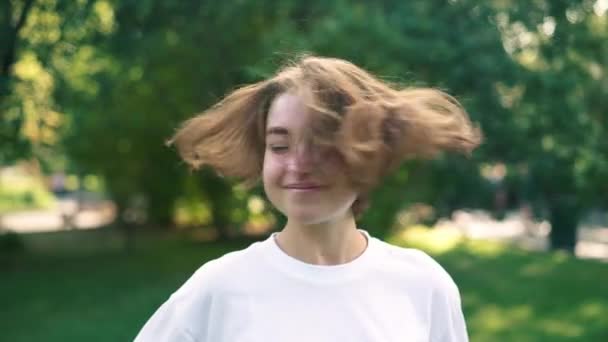 Mladá dívka s krátké světlé vlasy, hraje si s nimi v létě parku — Stock video