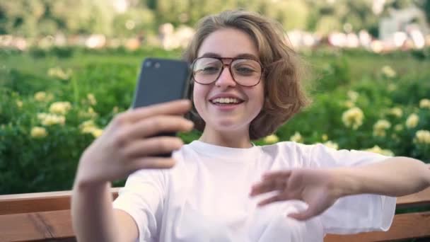 Aranyos fiatal lány szemüveg video hívás vagy vlogging nyári Park — Stock videók