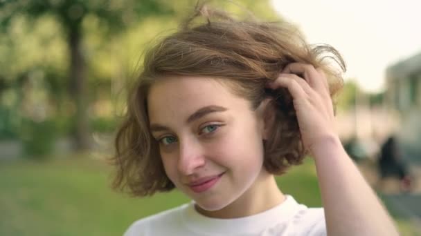 Roztomilá mladá žena s úsměvem a mrkl, při pohledu na fotoaparát v letním parku — Stock video