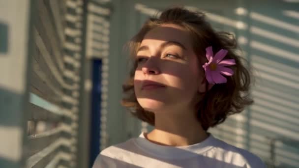 Hermosa mujer joven con flor en el pelo se ve de lado, a continuación, se convierte en cámara — Vídeos de Stock