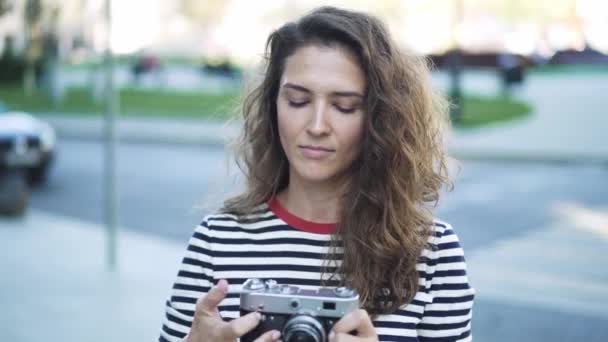 Beautiful young tourist with long curly hair taking a shot with a vintage camera — Stock Video