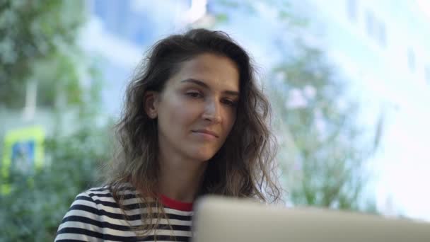 Junge Frau blickt im Sommercafé auf Laptop-Bildschirm — Stockvideo