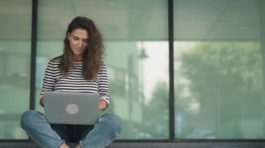 Çapraz bacaklı laptopunu merdivenleri bina ile yazarak ciddi genç kadın