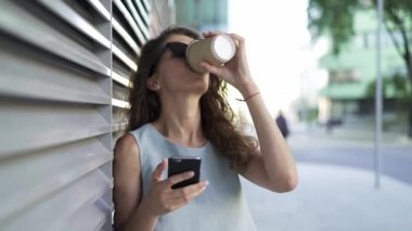 Kahve ve web sörf ayakta gri duvarının yakınında yaz şehirde içme kadın