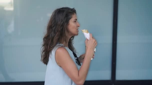 Vista laterale della bella giovane donna che mangia e beve caffè mentre cammina — Video Stock