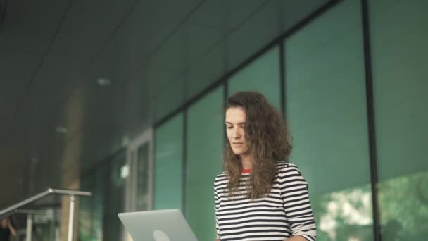 Mujer joven con camisa a rayas usando su computadora portátil fuera, inclinar hacia abajo — Vídeo de stock