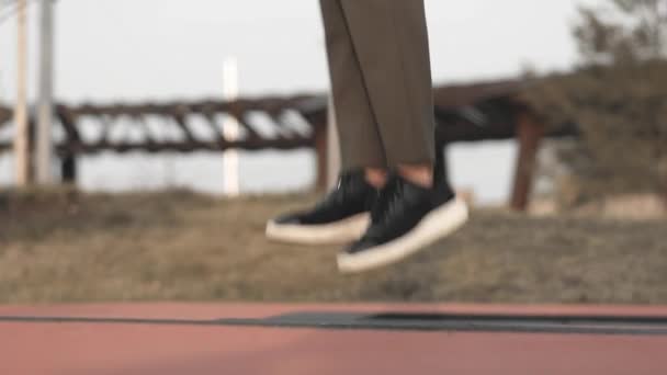 Piernas de mujer en pantalones caqui y zapatillas de deporte saltando en el trampolín en el parque — Vídeos de Stock