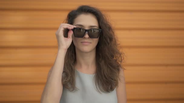 Belle jeune femme enlève des lunettes de soleil et sourit à l'extérieur — Video