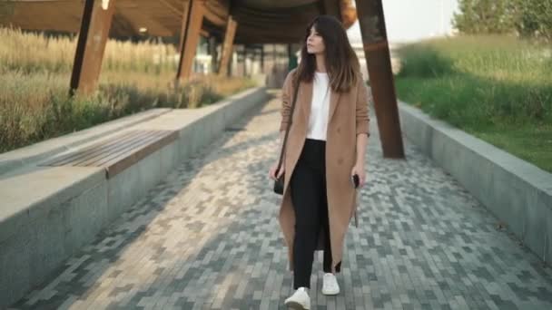 Hermosa joven morena caminando en el parque de otoño y sonriendo mirando a su alrededor — Vídeo de stock