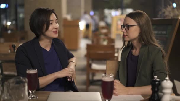 Dos amigas jóvenes hablando en la cafetería al aire libre de noche — Vídeos de Stock