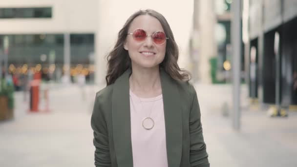 Attraente giovane donna sorridente e guardando la fotocamera in piedi in strada della città — Video Stock