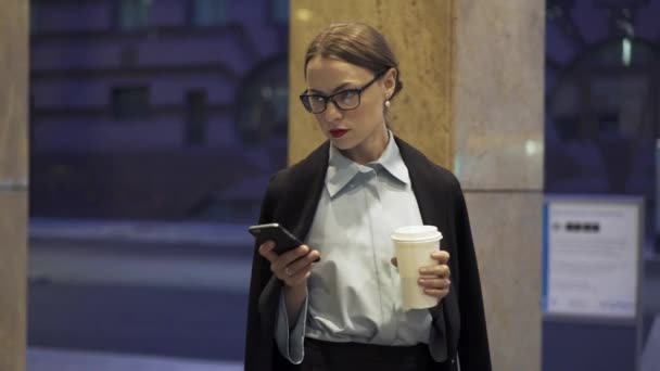 Mujer de negocios con café caminando y navegando por la red oh su teléfono inteligente — Vídeos de Stock