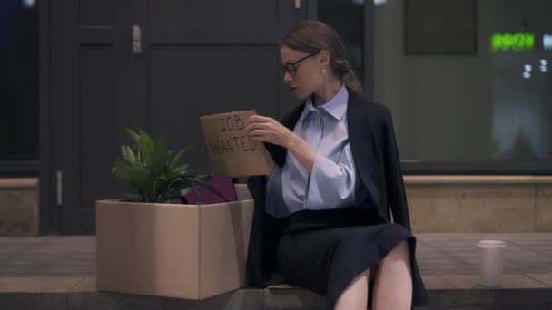 Mujer joven sacando trabajo quería cartel de cartón sentado en la calle de la noche — Vídeo de stock