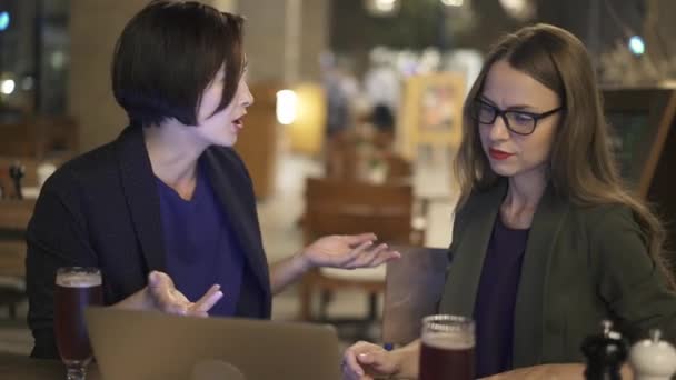 Duas jovens mulheres fechando laptop e bebendo cerveja no café à noite — Vídeo de Stock