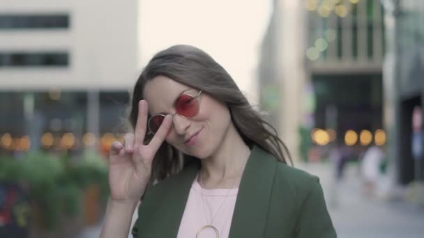 Muchacha bastante joven mostrando signo de victoria en una calle de otoño — Vídeos de Stock