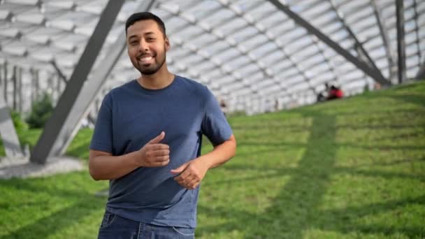 Hombre hispano sonriente bailando en un césped verde en un día soleado — Vídeos de Stock