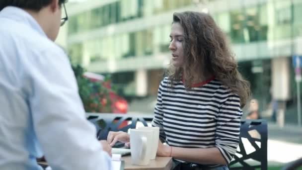 Dos jóvenes colegas trabajando en caffe de verano con portátil y portapapeles — Vídeo de stock