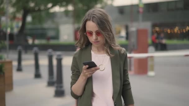 Young businesswoman dialing a number and talking walking in fall city street — Stock Video
